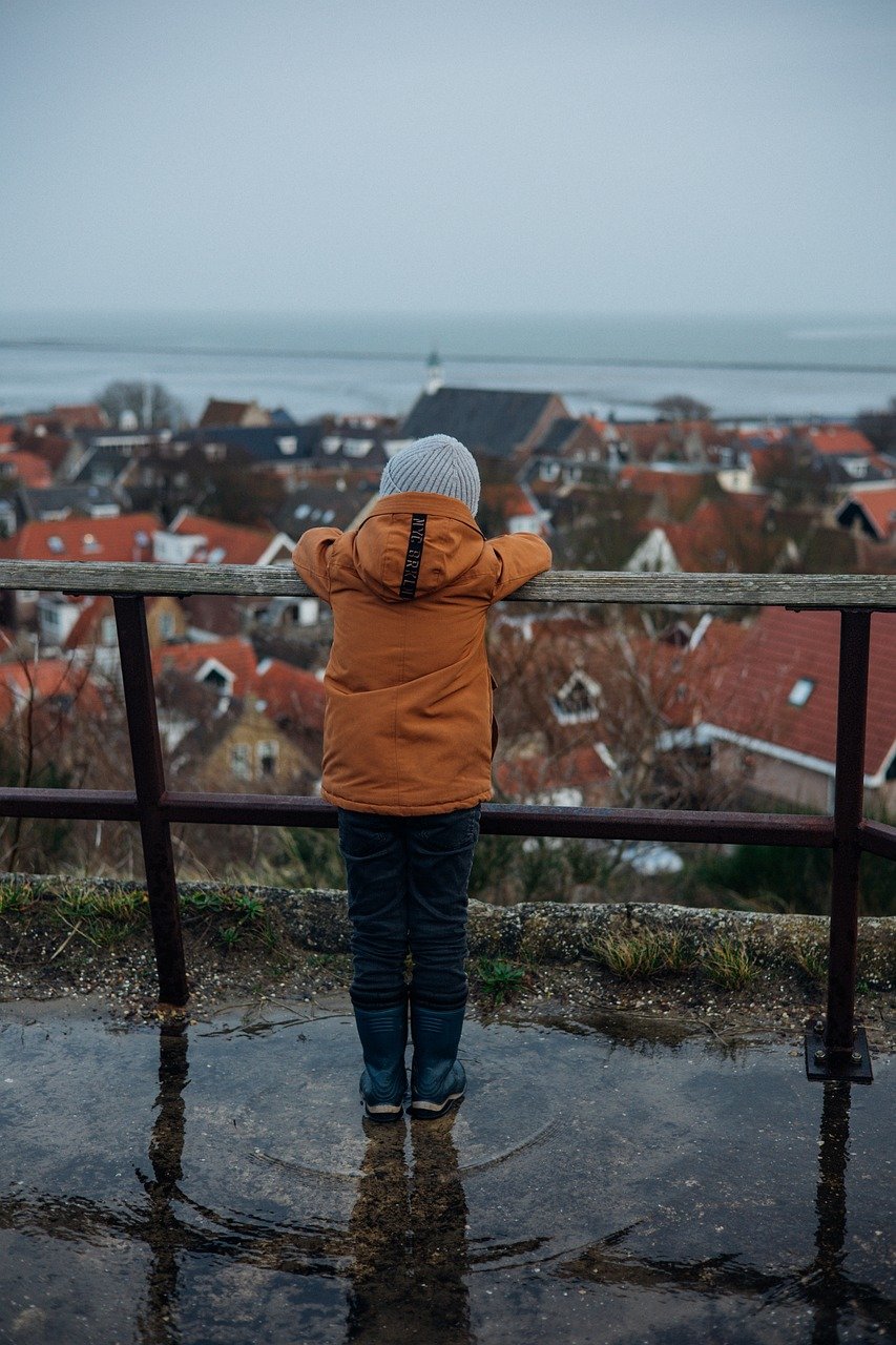 Chłopiec opierający się o poręcz patrzący na panoramę miasta w deszczowy dzień